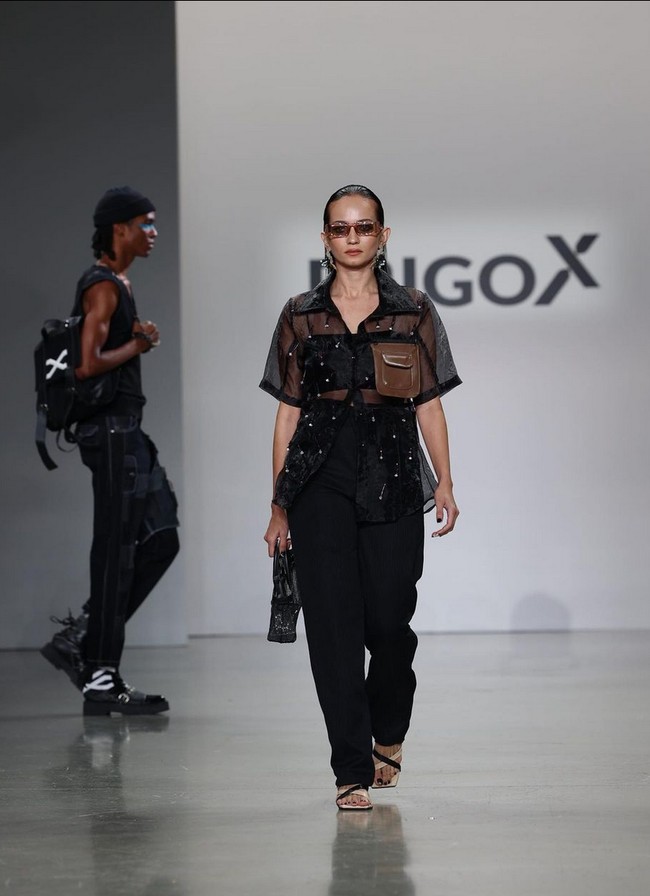 Enzy Storia tampil simpel dalam balutan kemeja transparan yang dipadu crop top, celana hitam serta sepatu sandal. Rambutnya ditata sleek ke belakang sementara wajah dipulas makeup dengan efek glossy. Foto: Instagram/@erigostore