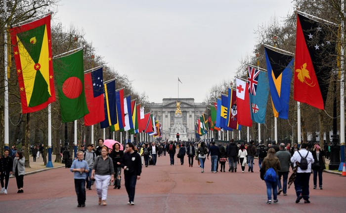 Pedestrians walk underneath flags of Commonwealth countries flying from flag poles along the Mall leading to Buckingham Palace in central London  on April 15, 2018 ahead of the opening of the biennial Commonwealth Heads of Government Meeting (CHOGM). - The 53 member states are gathering for their biennial Commonwealth Heads of Government Meeting (CHOGM), being hosted this year in London. (Photo by Ben STANSALL / AFP)