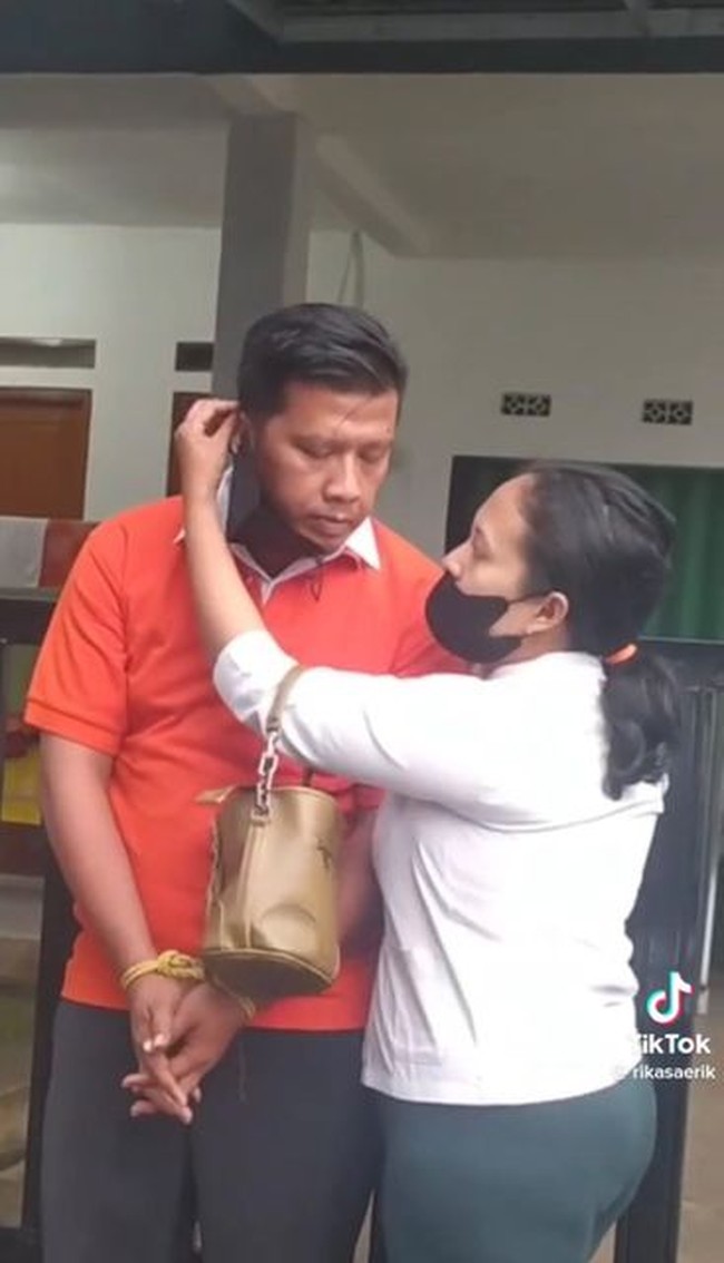 Dalam video viral terlihat sang suami meniru gaya Ferdy Sambo yang tangannya sedang terikat dilengkapi dengan kaus oranye ala tahanan.  Sedangkan sang istri memakai kemeja putih dan membawa tas. Ia juga meniru gaya Putri Candrawathi yang memasangkan masker untuk suami.  Foto: Dok. TikTok @rikasaerik.