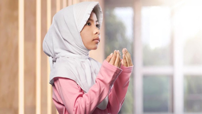 Portrait of asian muslim child raising hand and praying in the mosque