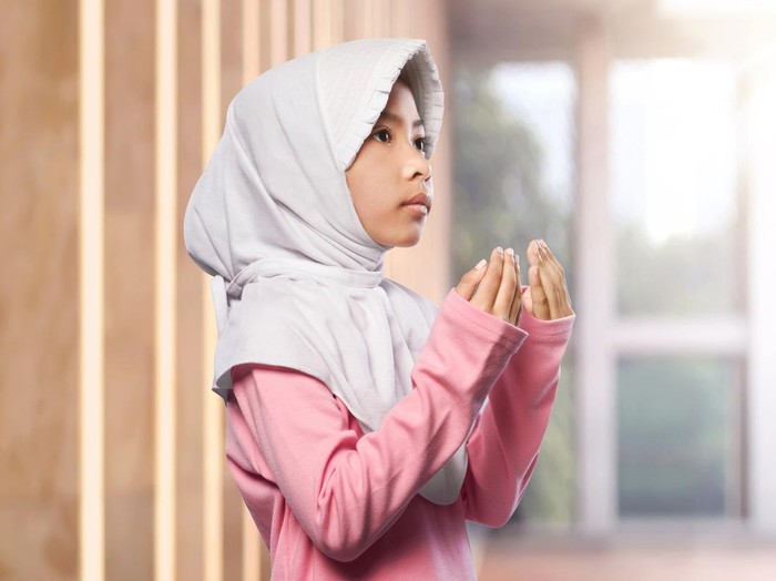 Portrait of asian muslim child raising hand and praying in the mosque