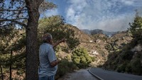 Seorang warga melihat kebakaran hutan di pinggir jalan raya. Terlihat api yang mulai mendekati jalan raya.
