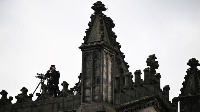 Penampakan Penembak Jitu Siap Siaga di Pemakaman Ratu Elizabeth II Police officers with snipers stand on the roof of the St Giles' Cathedral in Edinburgh on September 11, 2022, where Queen Elizabeth II will lie at rest and ahead of the ceremony of the proclamation of Britain's King Charles III. - Queen Elizabeth II's coffin will travel by road through Scottish towns and villages on Sunday as it begins its final journey from her beloved Scottish retreat of Balmoral. The Queen, who died on September 8, will be taken to the Palace of Holyroodhouse before lying at rest in St Giles' Cathedral, before travelling onwards to London for her funeral. (Photo by Oli SCARFF / AFP) (Photo by OLI SCARFF/AFP via Getty Images)