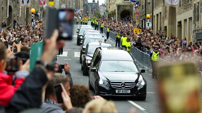People watch the Queens cortege with the hearse containing her coffin on the Royal Mile in Edinburgh, Scotland, Sunday, Sept. 11, 2022. The coffin of the late Queen Elizabeth II is being transported Sunday on a journey from Balmoral to the Palace of Holyroodhouse in Edinburgh, where it will lie at rest before being moved to London later in the week. (AP Photo/Petr David Josek)