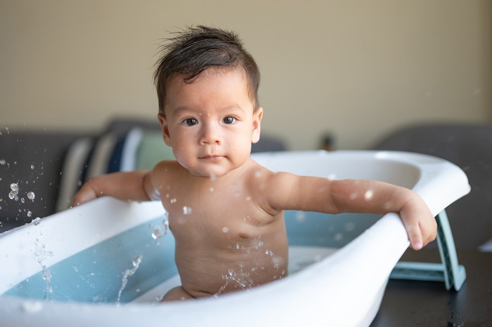 Adorable six moths old mixed race baby boy taking a bath in a small baby tub in the living room splashing water excitedly