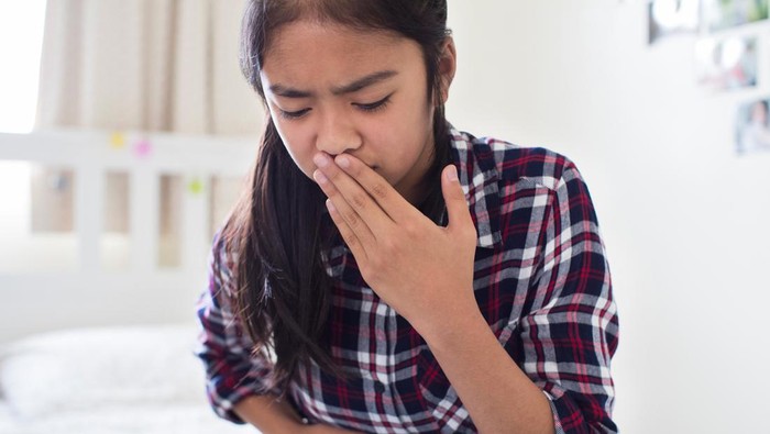 Young Girl Sitting On Bed At Home Feeling Nauseous