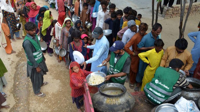 TOPSHOT - Displaced flood-affected people stand in a queue to receive food being distributed by Saylani Welfare Trust at a makeshift camp in flood-hit Sehwan of Sindh province on September 13, 2022. (Photo by Husnain ALI / AFP) (Photo by HUSNAIN ALI/AFP via Getty Images)