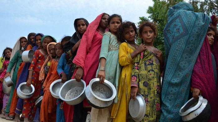 TOPSHOT - Displaced flood-affected people stand in a queue to receive food being distributed by Saylani Welfare Trust at a makeshift camp in flood-hit Sehwan of Sindh province on September 13, 2022. (Photo by Husnain ALI / AFP) (Photo by HUSNAIN ALI/AFP via Getty Images)