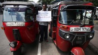Seorang pengemudi berdiri di tengah bajaj yang sedang parkir di pinggir jalan dengan membawa poster bertuliskan tolak kenaikan harga BBM, di Kolombo, Rabu (14/9/2022). (Pradeep Dambarage/Getty Images)