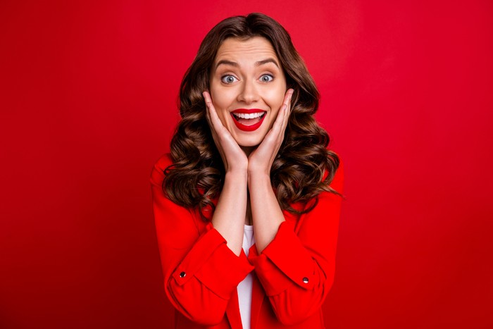 Pretty lady with open mouth hold, arms on cheekbones wear formal-wear red jacket isolated burgundy background