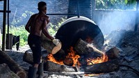 Pekerja membakar batang pohon untuk memasak kedelai. Proses pembuatan tahu ini masih menggunakan cara tradisional.
