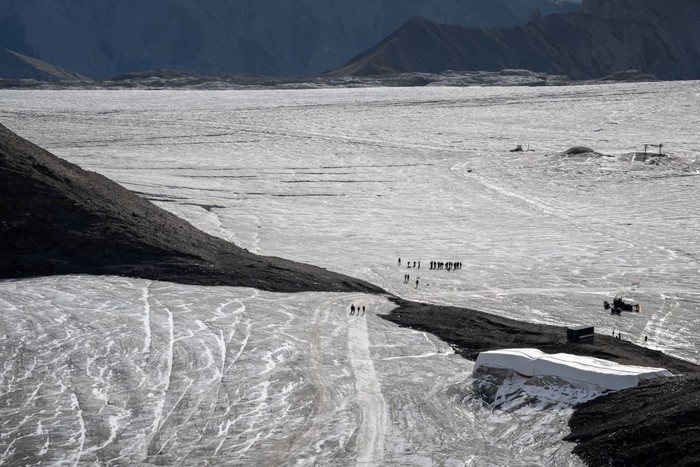 This picture taken on September 13, 2022 at the Glacier 3000 resort above Les Diablerets shows tourists walking on the Tsanfleuron pass free of the ice that covered it for at least 2,000 years. - The thick layer of ice that has covered a Swiss mountain pass between Scex Rouge glacier and Tsanfleuron glacier since at least the Roman era has melted away completely. Following a dry winter, the summer heatwaves hitting Europe have been catastrophic for the Alpine glaciers, which have been melting at an accelerated rate. (Photo by Fabrice COFFRINI / AFP) (Photo by FABRICE COFFRINI/AFP via Getty Images)