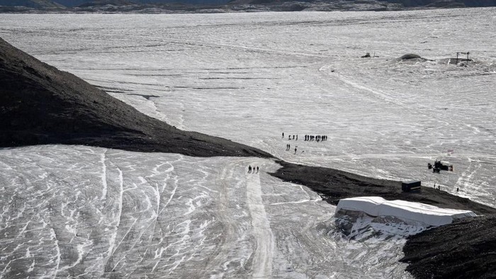 Duh, Lapisan Es di Celah Pegunungan Swiss Mencair This picture taken on September 13, 2022 at the Glacier 3000 resort above Les Diablerets shows tourists walking on the Tsanfleuron pass free of the ice that covered it for at least 2,000 years. - The thick layer of ice that has covered a Swiss mountain pass between Scex Rouge glacier and Tsanfleuron glacier since at least the Roman era has melted away completely. Following a dry winter, the summer heatwaves hitting Europe have been catastrophic for the Alpine glaciers, which have been melting at an accelerated rate. (Photo by Fabrice COFFRINI / AFP) (Photo by FABRICE COFFRINI/AFP via Getty Images)