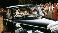Momen saat Ratu Elizabeth II mengantarkan anak-anaknya Pangeran Charles dan Putri Anne di Windsor. Aksi Ratu menyetir mobil itu disaksikan oleh sekelompok penonton, 1957. (© Hulton-Deutsch Collection/CORBIS/Getty Images)