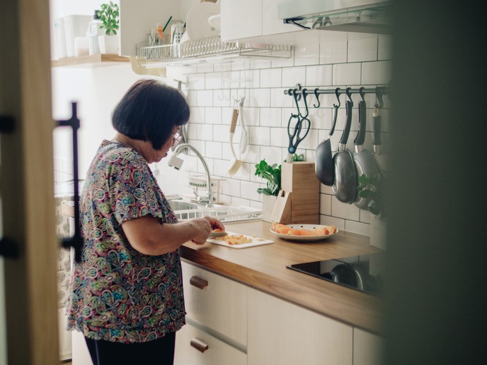 Asian grandmother hands sliced orange in kitchen at home.