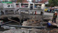 Beton tersusun di pinggir jalan. Terlihat pekerja yang sedang menyelesaikan pengerjaan saluran air.