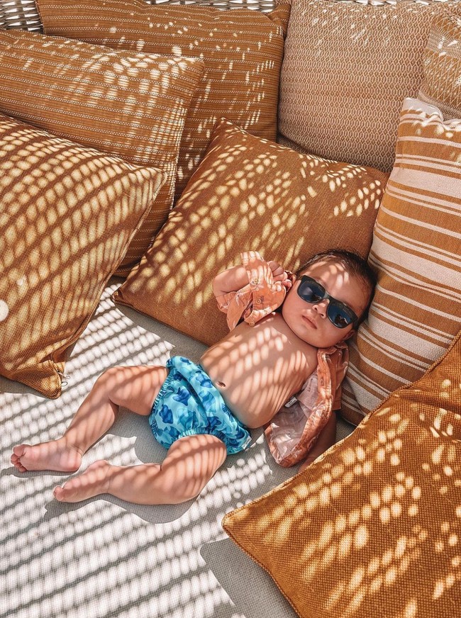 Tak hanya bermain pasir dan berenang, baby Izz juga tampak berjemur sambil menikmati suasana pantai di Yunani. Mengenakan kaca mata hitam, celana biru bermotif dan kemeja oranye yang tak dikancing, penampilan baby Izz sukses bikin gemas. Foto: Instagram/@indpriw