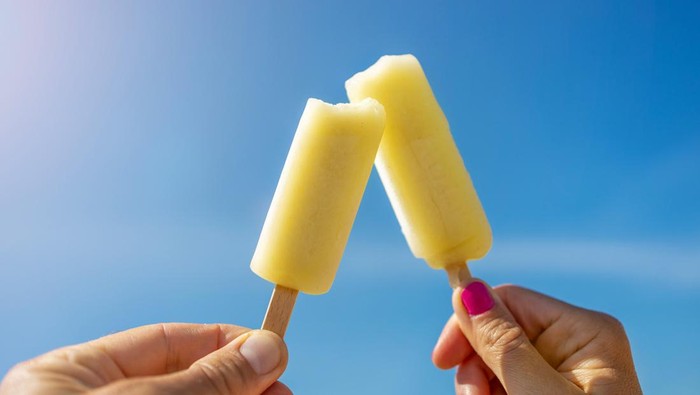 Hands Holding Popsicles Against Blue Sky