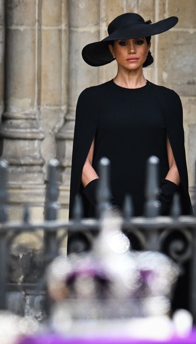 Meghan Markle juga menonjolkan aura elegannya dengan gaun hitam bersiluet lurus yang dilengkapi cape dan sarung tangan senada. Sebuah topi juga dipakainya dengan ukuran yang lebih besar dari milik Kate. (Foto: AFP via Getty Images/OLI SCARFF)
