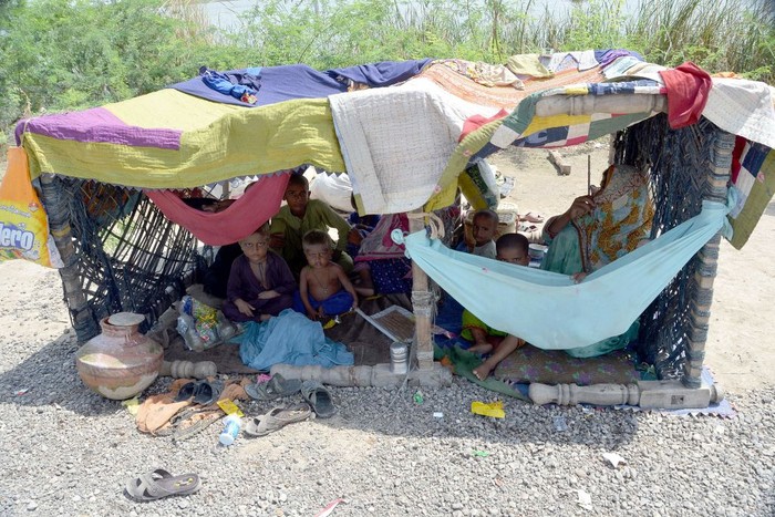 1243358332 A flood-affected family sits inside a temporary tent in a makeshift camp at Sohbatpur in Jaffarabad district of Balochistan province on September 19, 2022. (Photo by Fida HUSSAIN / AFP) (Photo by FIDA HUSSAIN/AFP via Getty Images)