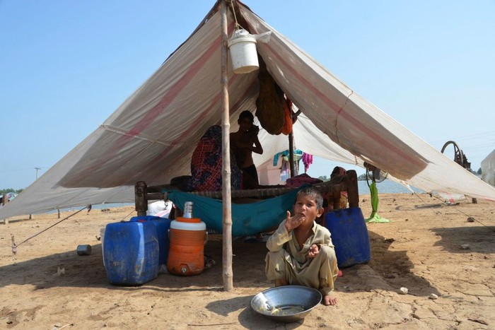 1243358332 A flood-affected family sits inside a temporary tent in a makeshift camp at Sohbatpur in Jaffarabad district of Balochistan province on September 19, 2022. (Photo by Fida HUSSAIN / AFP) (Photo by FIDA HUSSAIN/AFP via Getty Images)