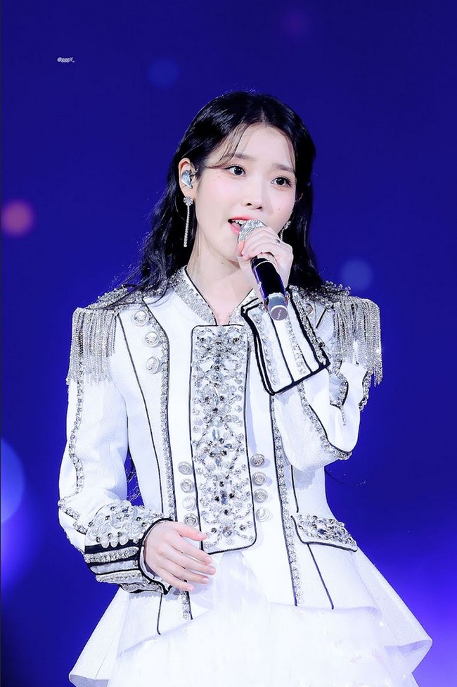 Salah satu gayanya yang jadi perbincangan adalah ala militer berikut ini. IU mengenakan atasan berkesan maskulin dipadukan dengan dress bernuansa peach yang kontras sehingga unik. Foto: Dok. Fansite Blueming