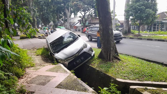 Mobil masuk ke parit di Jl Ahmad Yani, Bogor, sejak Senin (19/9) malam belum dievakuasi hingga jadi tontonan warga.