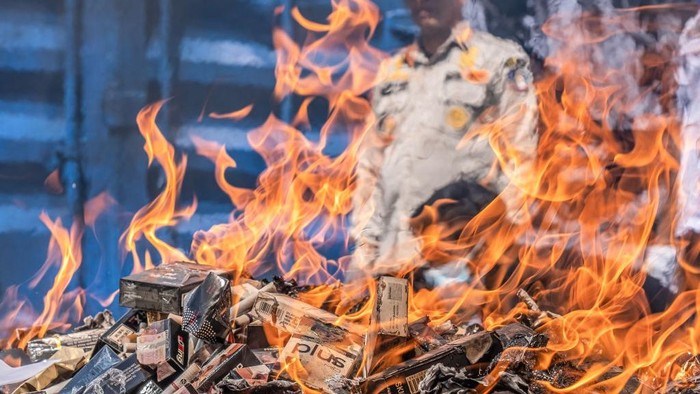 KENDARI, SOUTH EAST SULAWESI, INDONESIA - 2022/09/21: Officers throw cigarettes into containers for the destruction of evidence by burning. Kendari Customs, in the period July to September 2022, takes action against excisable goods that do not meet the provisions of the law originating from targeting illegal market operations, and land and sea patrols for smuggled goods. The contraband resulting from the prosecutions are then designated state property (BMN) and they have received approval from the Office of the State Property and Auction Service (KPKNL) to destroy the excisable goods. (Photo by Andry Denisah/SOPA Images/LightRocket via Getty Images)