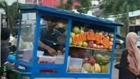 Roti bakar biasanya paling cocok dinikmati saat malam hari. Tak ingin kehilangan pelanggan, penjual ini menyulap gerobak roti bakarnya menjadi gerobak rujak buah yang menyegarkan saat siang hari. Foto: Twitter/nocontextwarung