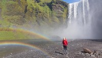 Seorang turis berdiri di depan air terjun Skógafoss di Skógar, Islandia. 