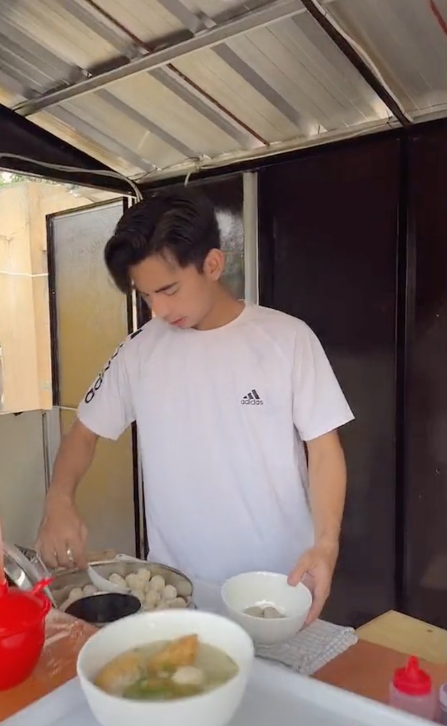 Dimas yang mengenakan kaos putih itu tampak dengan sigap langsung menyiapkan sendiri bakso jualannya. Ia pun terlihat ramah kepada pembeli baksonya tersebut. Foto: TikTok/@montcan