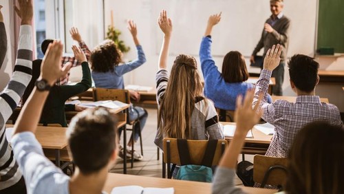 Rear view of large group of students raising their hands to answer the question on a class.