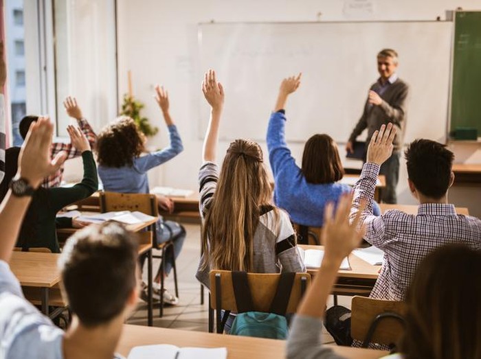 Rear view of large group of students raising their hands to answer the question on a class.