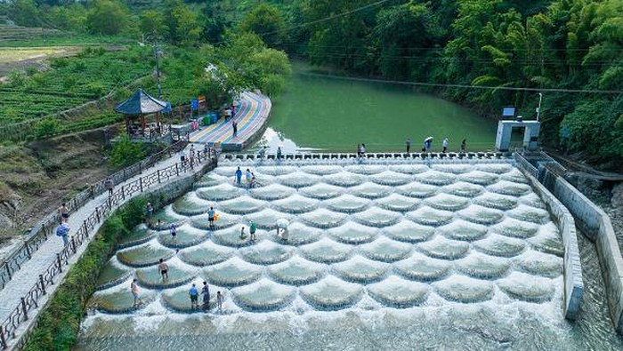 Penghalang Arus Sungai di China Bentuknya Sisik Ikan, Cocok Buat Foto-foto XIANFENG, CHINA - JULY 28: Tourists cool off at a location known for fish scale-shaped barriers that form small waterfalls during a hot summer day on July 28, 2022 in Xianfeng County, Enshi Tujia and Miao Autonomous Prefecture, Hubei Province of China. (Photo by Ye Xingjian/VCG via Getty Images)