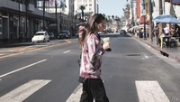 Enzy terlihat menyebrangi jalanan di Hollywood Walk Of Fame sambil menyeruput minuman matcha.  Foto: Instagram @enzystoria
