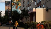 Seorang wanita berjalan di sepanjang jalan dengan mural yang dipajang di blok apartemen bertingkat yang terlihat di latar belakang selama festival internasional Urban Morphogenesis, yang diadakan di kota Balashikha di luar Moskow, Rusia, Selasa, (20/9/2022).