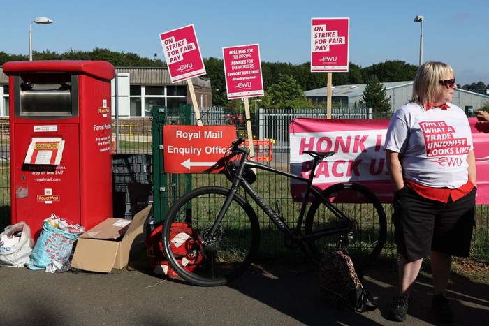 1242724475 TOPSHOT - A Royal Mail postal worker stands at a picket line outside the Basingstoke delivery office on August 26, 2022 during a strike over pay. - The Royal Mail Basingstoke delivery office had a 100 percent turnout for the nationwide strike with each of its 220 workers, all members of the Communication Workers Union (CWU), taking part. (Photo by Adrian DENNIS / AFP) (Photo by ADRIAN DENNIS/AFP via Getty Images)