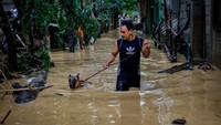 Seorang warga yang membawa anjing peliharaannya melintasi jalanan yang terendam banjir setinggi paha.