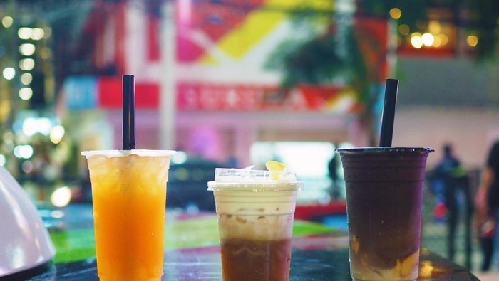 Plastic glasses of iced grapefruit green tea, oolong tea,  dark cocoa with layer of cream cheese foam ; Traditional Chinese Beverage. Selective focus.