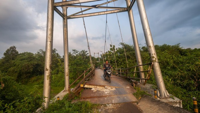 Pengendara  sepeda motor melintasi jembatan gantung yang rusak di Rangkasbitung, Lebak, Banten, Minggu (25/9/2022). Jembatan tersebut konstruksi telah miring dan sebagian besinya mengalami kerusakan sehingga membahayakan bagi yang melintas. ANTARA FOTO/Muhammad Bagus Khoirunas/tom.