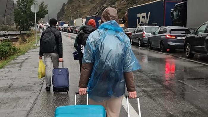 People carrying luggage walk past vehicles with Russian license plates on the Russian side of the border towards the Nizhniy Lars customs checkpoint between Georgia and Russia some 25 km outside the town of Vladikavkaz, on September 25, 2022. - Russian authorities acknowledged a 