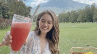 Lebih cantik mana nih? Wajah Dhyaz saat tersenyum lebar atau pemandangan pikniknya? Ia juga melengkapi momen ini dengan minum segelas jus buah segar. 