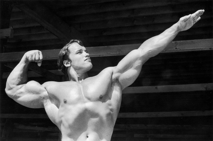 circa 1966:  Austrian-born bodybuilder Arnold Schwarzenegger points one hand out as he flexes his torso on Muscle Beach, Santa Monica, California.  (Photo by Hulton Archive/Getty Images)