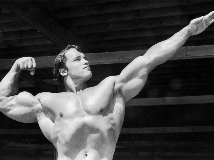 3238896 circa 1966: Austrian-born bodybuilder Arnold Schwarzenegger points one hand out as he flexes his torso on Muscle Beach, Santa Monica, California. (Photo by Hulton Archive/Getty Images)