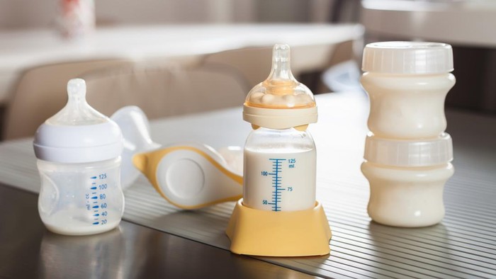 Baby bottle with milk and manual breast pump. A lot of full bottles with breast milk on the background. Mothers milk - the most healthy food for newborn