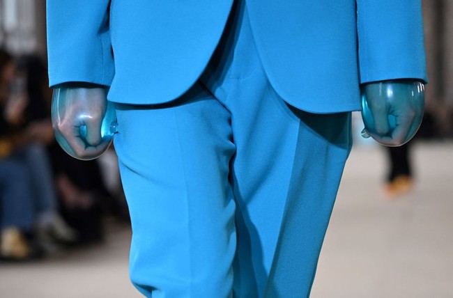 Air merupakan elemen utama yang jadi inspirasi busana berpotongan tailoring ini. Salah satunya ditampilkan oleh model yang mengenakan setelan celana panjang dan blazer dengan kedua tangan terbungkus sarung tangan bernuansa aquatik. Foto: Getty Images