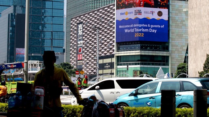 Warga melintas di dekat layar yang menampilkan iklan tiket.com di Jakarta, Selasa (27/9/2022).