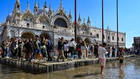 Turis berjalan melintasi jalan setapak yang ditinggikan saat terjadi banjir pasang di luar Basilika St Markus, alun-alun St Mark, Venesia, Italia.