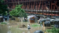 Warga berdiri di tengah banjir. Telihat juga banyak sampah yang mengapung di tengah banjir tersebut.