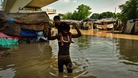Seorang warga menggendong anaknya di tengah banjir.